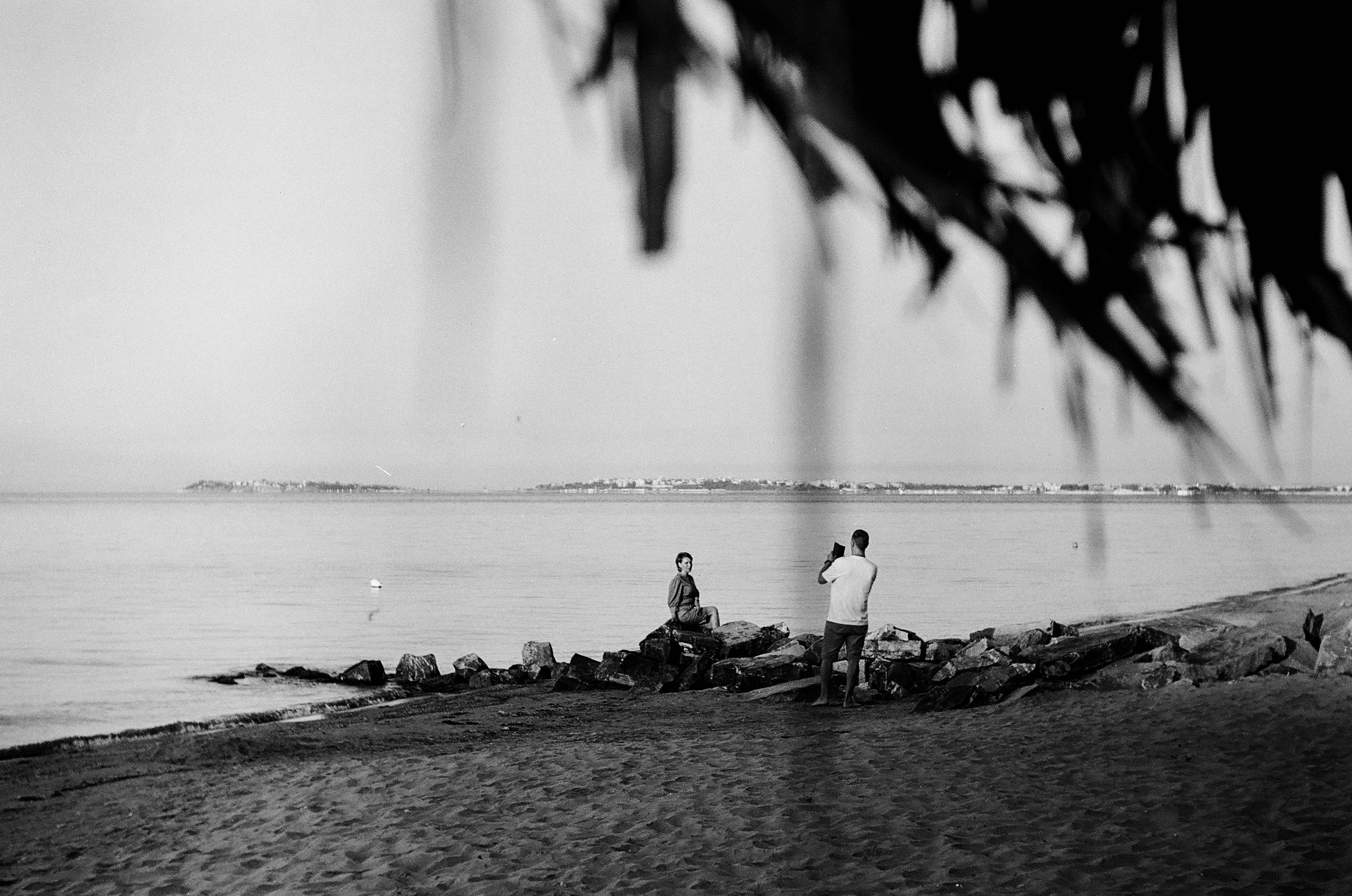 grayscale photo of people sitting on rock near water fountain